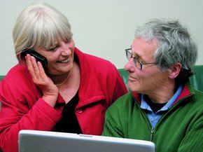 Starejši par pred prenosnikom, gledata se, medtem ko se ženska pogovarja po telefonu